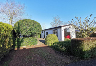 Cabaña moderna Chalet Basic en De Woudhoeve, Países Bajos, rodeada de setos bien cuidados y árboles.