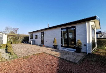 Udendørsbillede af Chalet Basic, et moderne hvidt bjælkehus med sort tag, terrasse og have under klar himmel.