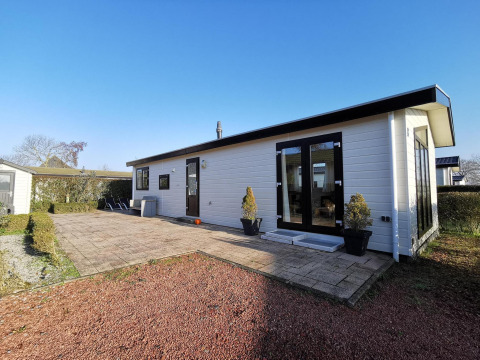 Vue extérieure du Chalet Basic, une cabane blanche avec terrasse, plantes et ciel bleu dégagé.