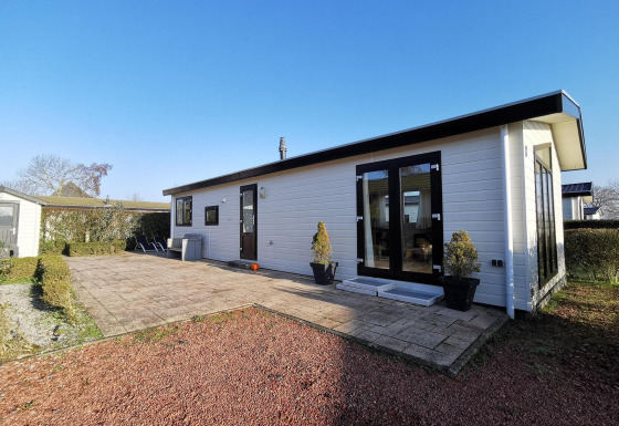 Vue extérieure du Chalet Basic, une cabane blanche avec terrasse, plantes et ciel bleu dégagé.