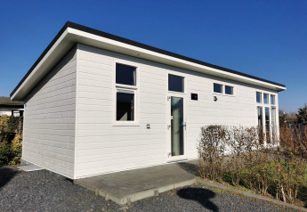 Chalet Basic ved De Woudhoeve i Holland ses med hvide vægge, store vinduer og skråt tag under blå himmel.