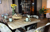 Eethoek in safaritent met bloemrijke stoelen, houten tafel, keramieken bekers en houten wand.