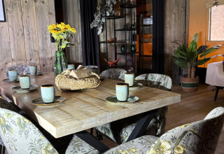 Eethoek in een safaritent met bloemetjesstoelen, houten tafel, keramieken kopjes en houten muur.