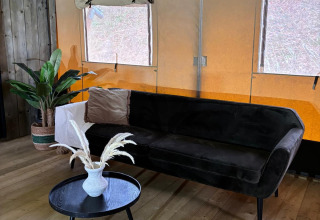 Safari tent interieur met zwarte zetel, klein tafeltje met vaas, plant en houten vloer, twee ramen.