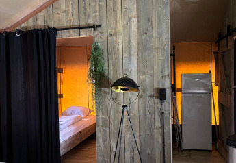 Innenaufnahme eines Safarizeltes mit Holzboden, Bettbereich mit Vorhang und Kühlschrank im Hintergrund.