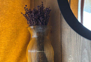 Een glazen vaas met gedroogde lavendel staat op een plank in een safaritent, met warm geel licht.
