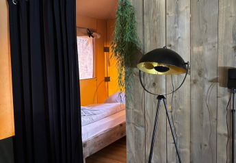 Innenaufnahme eines Safari-Zeltes mit Bett, schwarzen Vorhängen, Holzwänden und Stehlampe.