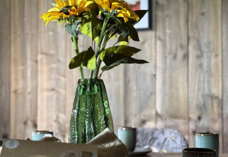 Gele zonnebloemen in groene vaas op houten tafel met kopjes en mand in een safari tent.