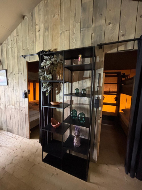 Interieur van een safaritent met zwarte open kast, decorstukken en twee slaapkamers met stapelbedden.