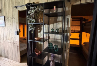 Interieur van een safaritent met zwarte open kast, decorstukken en twee slaapkamers met stapelbedden.