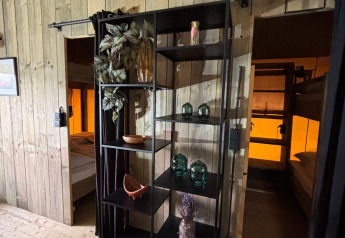 Safari-Zelt-Innenraum mit schwarzem Regal, Dekorationsobjekten und zwei Schlafbereichen mit Stockbetten.