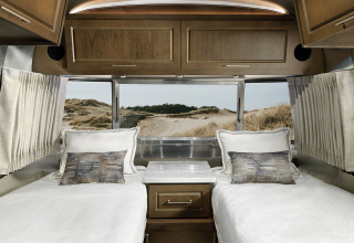 Binnenzicht van een Airstream tiny house met twee eenpersoonsbedden, houten kasten en duinen buiten.