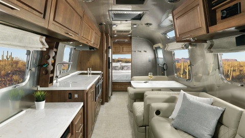 Moderne Airstream tiny house met houten kasten, sofa, eettafel en zicht op de woestijn.