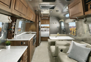 Moderne Airstream tiny house met houten kasten, sofa, eettafel en zicht op de woestijn.