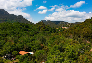 Vista aerea di verdi colline e foreste vicino a Fenouillet, Occitania, Francia, sotto un cielo azzurro nuvoloso.