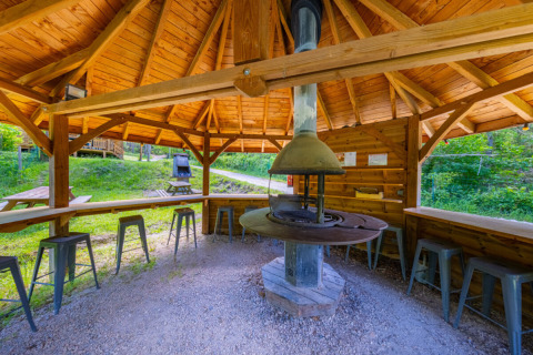 Padiglione in legno con barbecue centrale e sgabelli al Campeggio des Randonneurs in Occitania, Francia.