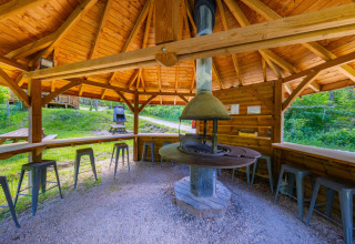Padiglione in legno con barbecue centrale e sgabelli al Campeggio des Randonneurs in Occitania, Francia.