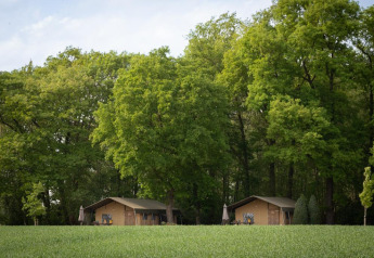 Tenda safari di lusso con bagno, immersa vicino a una foresta verde lussureggiante e campi aperti.