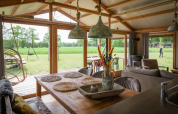 Innenraum einer luxuriösen Lodge mit Esstisch und Blick auf grüne Wiese in Landrijk de Reesprong, Niederlande.