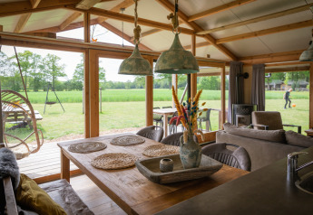 Innenraum einer luxuriösen Lodge mit Esstisch und Blick auf grüne Wiese in Landrijk de Reesprong, Niederlande.