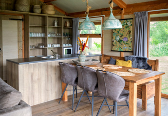 Interior de lodge de lujo con mesa de madera, cocina moderna y ventanales en Landrijk de Reesprong, Países Bajos.