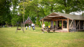 Una familia se divierte al aire libre junto a una lodge Luxe moderna entre naturaleza y zona verde.