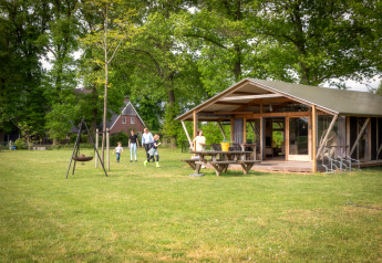 Familie entspannt vor einer Luxus-Lodge mit Veranda im Grünen und genießt die Natur.