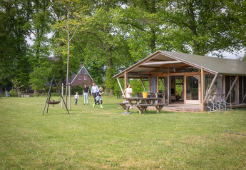 Familie entspannt vor einer Luxus-Lodge mit Veranda im Grünen und genießt die Natur.