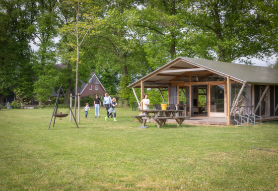 Famiglia si rilassa all’esterno di una Luxe lodge moderna con veranda tra alberi e prato verde.