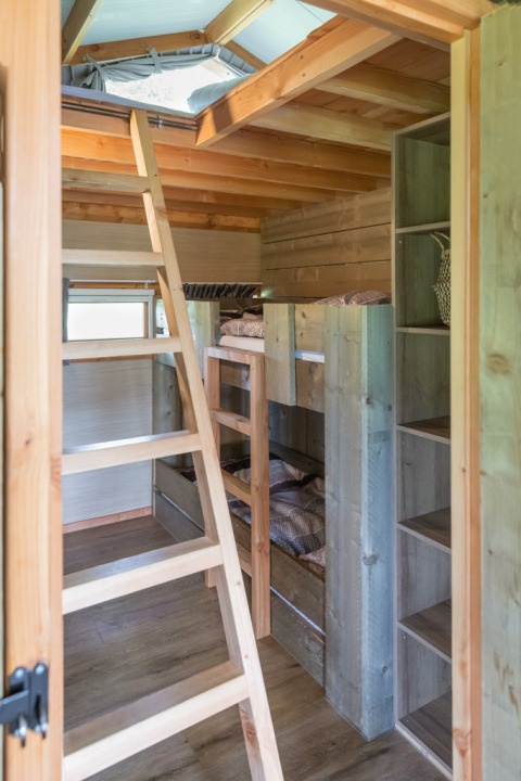 Innenraum der Luxe Lodge im Landrijk de Reesprong, Niederlande, mit Holzleiter, Etagenbetten und Oberlicht.