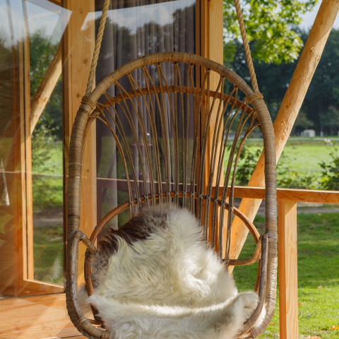 Hangende rotan stoel met schapenvacht op het terras van Luxe lodge incl oven bij Landrijk de Reesprong, Nederland.