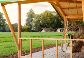 Udsigt fra træterrasse ved Luxe lodge incl oven på Landrijk de Reesprong, Holland, med grønne marker og hytter.