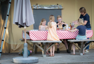 Kinder und Erwachsene essen gemeinsam an einem Tisch mit rotweißer Tischdecke im Safarizelt.