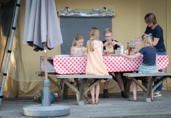 Bambini e un adulto mangiano insieme in una tenda safari di lusso con tovaglia a quadri nei Paesi Bassi.