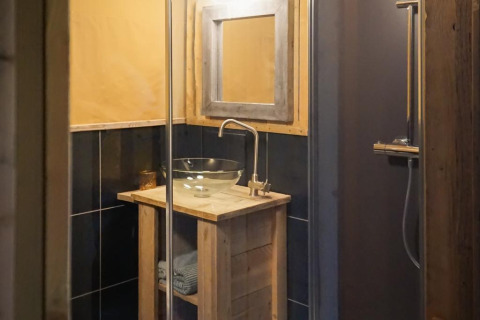 Baño de tienda safari de lujo en Landrijk de Reesprong, Holanda, con lavabo de vidrio y decoración rústica.