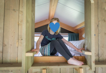 Niña jugando en una cabaña de madera en Luxe lodge, Landrijk de Reesprong, Países Bajos, ambiente acogedor.
