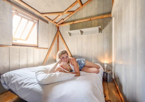 Young woman relaxing on a bed inside a cozy wooden cabin at Flower Camping Le Conleau, France.