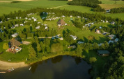 Aerial view of Campsite Hunze Bulten in Drenthe, Netherlands, featuring green fields and a lake.