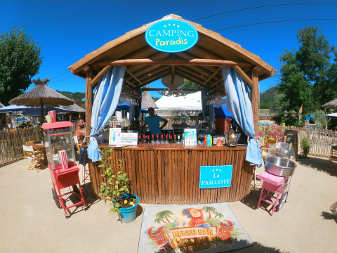 Zona de bar playero con carteles de Camping Paradis Family des Issoux en Auvergne-Rhône-Alpes, Francia.