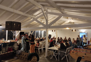 Group of people sharing dinner in a cozy, well-lit lodge at Family's Camping Le Savoy holiday park, France.