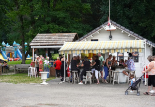 Gruppo di persone al chiosco di Family's Camping Le Savoy in Auvergne-Rhône-Alpes con parco giochi sullo sfondo.