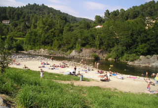 Personas descansando en la playa fluvial del Camping Paradis Family des Issoux rodeados de colinas verdes.