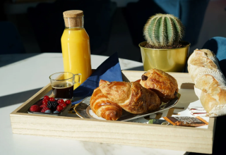 Morgenmad med croissanter, frugt, kaffe, appelsinjuice og baguette på bakke ved Family's Camping Le Savoy.