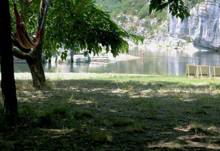 Schaduwrijke plek met hangmat, stoelen en rivier bij Camping Paradis Family des Issoux in Auvergne, Frankrijk.