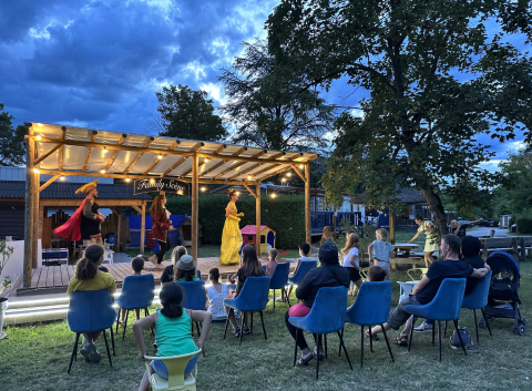 Escena de espectáculo familiar al aire libre al atardecer en Family's Camping Le Savoy, con público sentado.