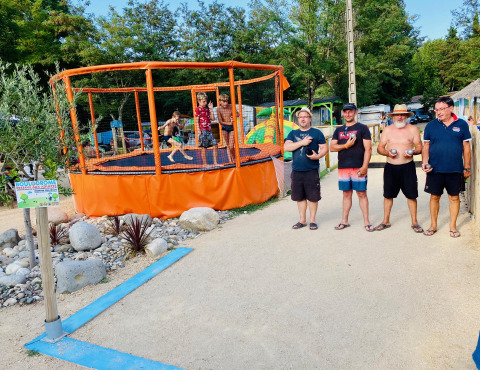 Quattro uomini accanto a un campo da bocce e bambini sul trampolino a Camping Paradis Family des Issoux, Francia.