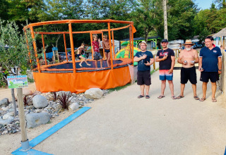 Quattro uomini accanto a un campo da bocce e bambini sul trampolino a Camping Paradis Family des Issoux, Francia.