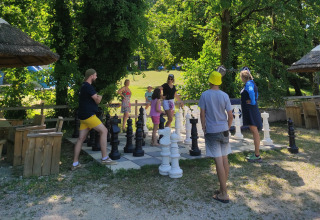 Familias juegan al ajedrez gigante al aire libre en un parque vacacional verde y soleado de Francia.