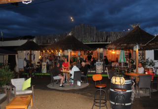 Atardecer en Camping Paradis Family des Issoux con huéspedes disfrutando en la terraza iluminada en Auvernia, Francia.