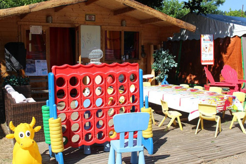 Udendørs legeområde for børn med legehus, stole, stort spil og farverige borde på Camping Paradis Family des Issoux.
